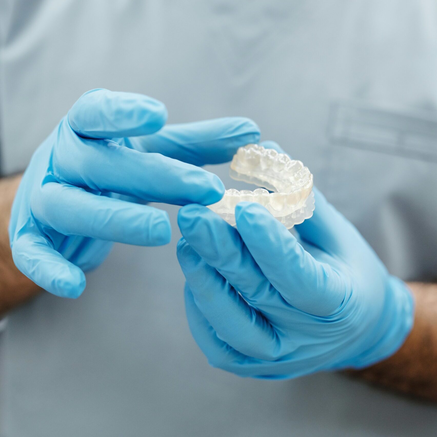 Dentist wearing blue gloves examining a dental mold in a clinical setting.